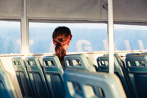 A young woman is sitting by herself on a ferry