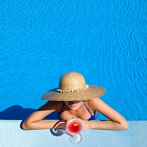 Woman in hat relaxing at the pool with cosmopolitan cocktail