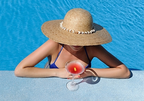 Woman in hat relaxing at the pool with cosmopolitan cocktail