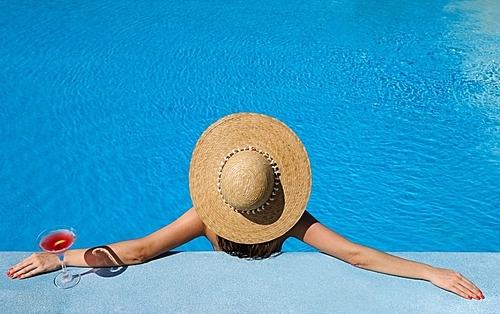 Woman in hat relaxing at the pool with cosmopolitan cocktail