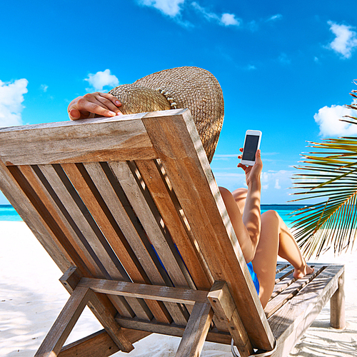 Young woman in hat with mobile phone at the beach