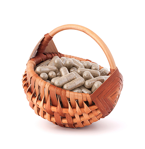 Herbal drug capsules in wicker basket isolated on white cutout. Alternative medicine concept.