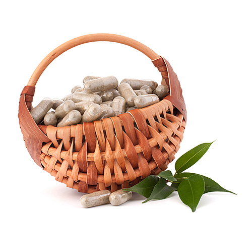 Herbal drug capsules in wicker basket isolated on white cutout. Alternative medicine concept.