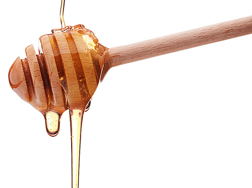 Honey dripping from a wooden honey dipper isolated on white cutout