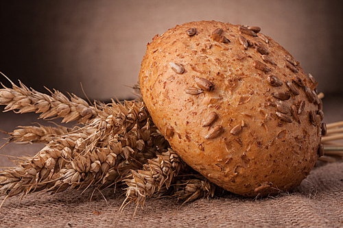 Loaf of bread and wheat ears still life on rustic background