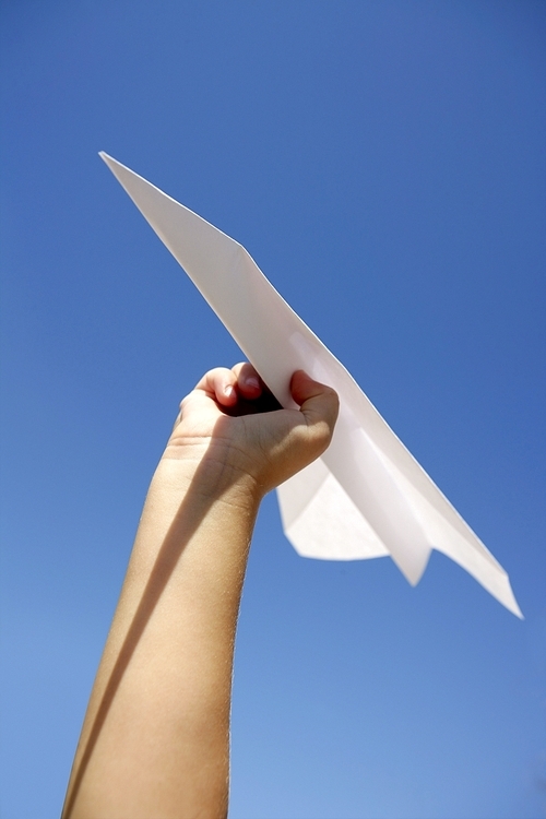 Paper airplane in children hand over blue sky