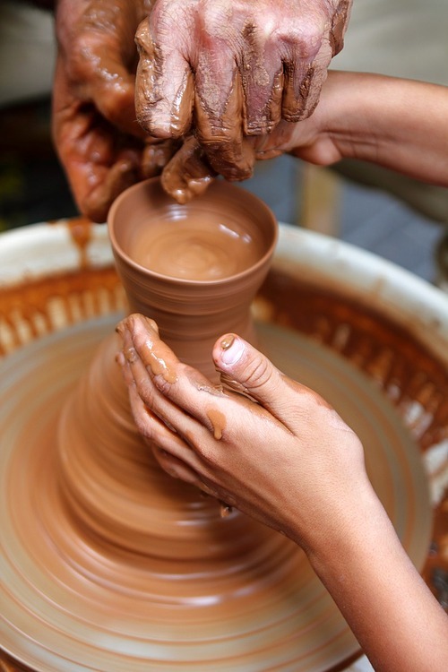 craftsman potter hands of teacher and pupil in a class clay pottery lesson