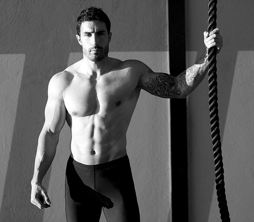 Crossfit gym handsome man holding hand a climbing rope