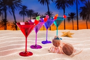 colorful cocktail in a row with cherry on sand beach palm trees sunset