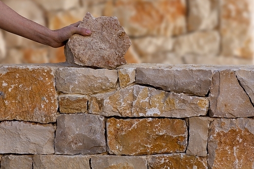 Mason hands working on masonry stone wall stonewall