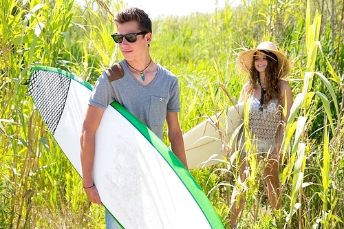 Surfer boy and girl walking in the green jungle with sunglasses