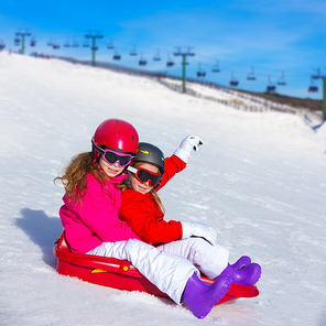 Kid girls playing sled in winter snow with helmets and goggles