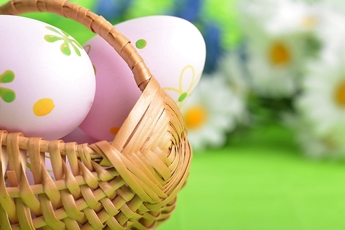 wicker basket of easter eggs with wildflowers on green background