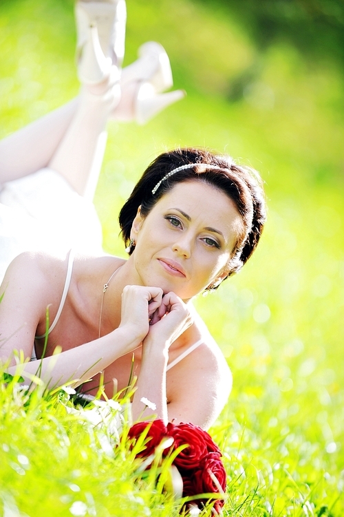 bride in white dress lying down in  grass.