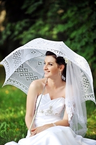 beautiful bride with umbrella sitting on the grass