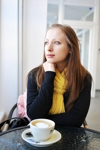 young woman sits at table in cafe. Drinks coffee