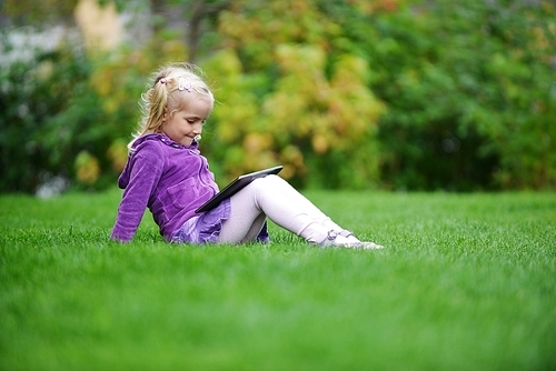 beautiful and happy little girl sitting on grass with laptop computer