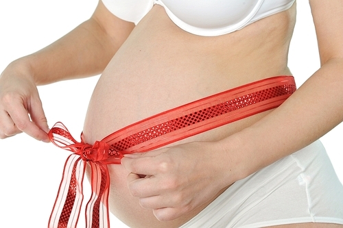 hands of  woman tied  red ribbon around  her pregnant belly