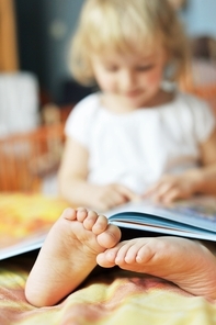 cheerful little girl with book sits on bed of parents
