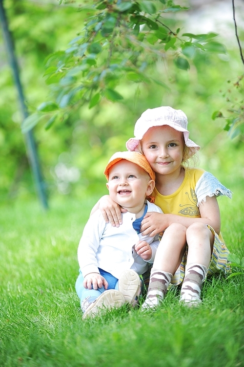 girl and her little brother sitting on  grass