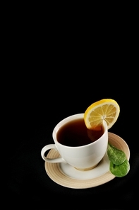 full cup of tea with lemon and  greens  leaves on  black