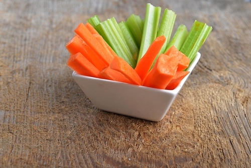 Bowl of carrot and celery sticks on wooden background