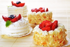 Small  cakes  with white icing and fruits on bamboo table cloth