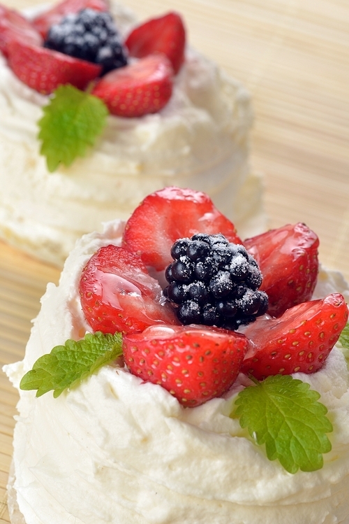 tasty cakes  with white icing and strawberries on bamboo table cloth