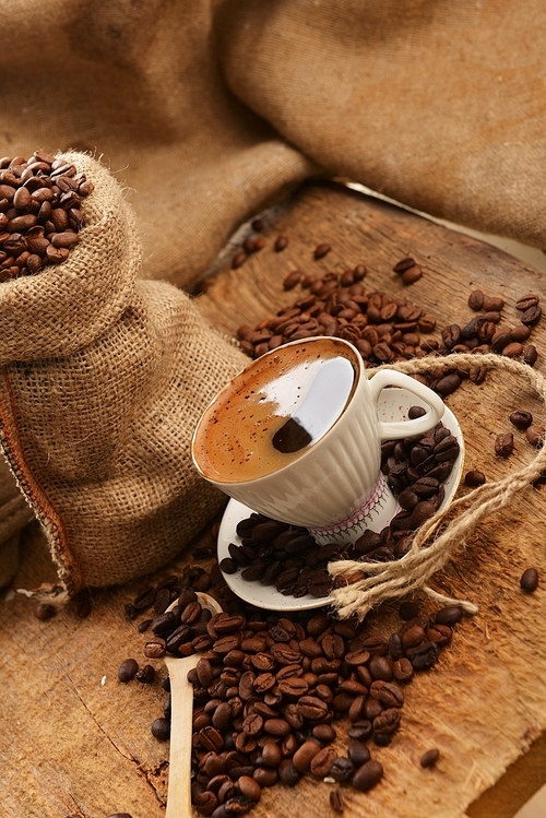 coffee beans in jute sack behind  cup of black coffee