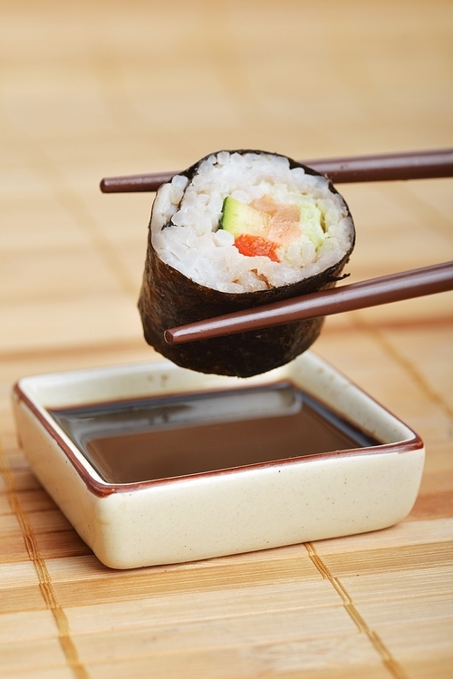 sushi between chopsticks ready to dip into  sauce