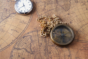 Vintage compass and a pocket watch lying on  old map