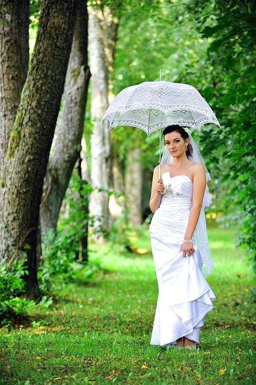 beautiful bride with umbrella walking in  park