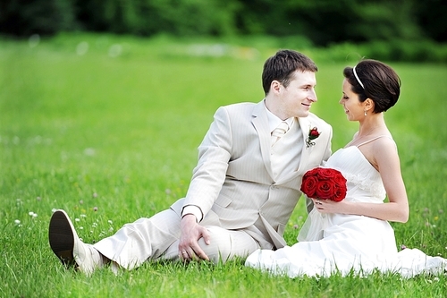 newly-married couple sit on  green grass in  field