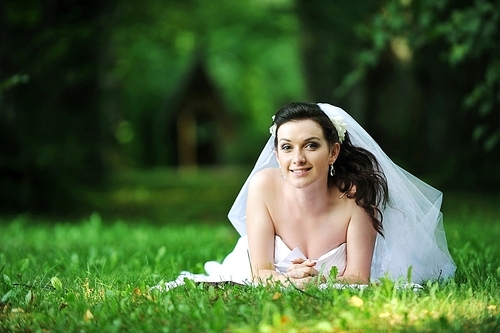 bride in white dress lying down in grass.