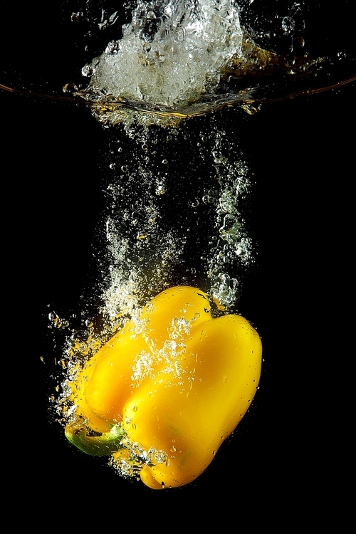 Colored yellow paprika in water splashes on black background