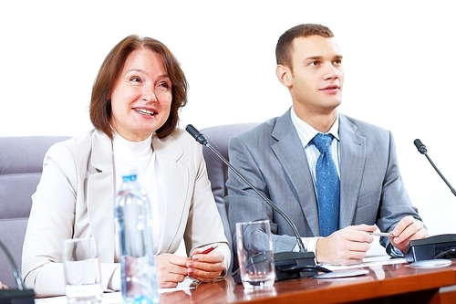 Image of two businesspeople sitting at table at conference speaking in microphone