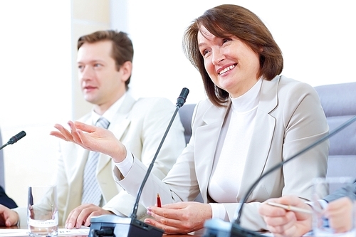 Image of two businesspeople sitting at table at conference speaking in microphone