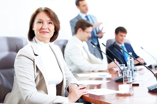 Image of businesswoman at business meeting with three businessmen in background