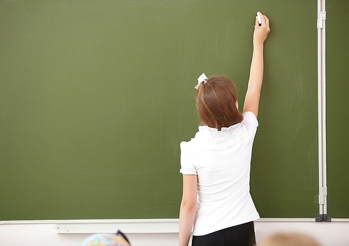 Scoolgirl standing in class near a green blackboard