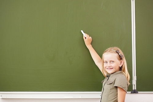 Scoolgirl standing in class near a green blackboard