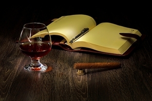 A glass with cognac|cigar and an old book nearby