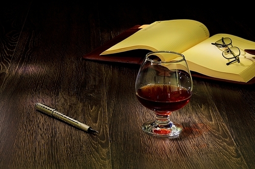 A glass with cognac|cigar and an old book nearby