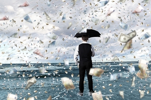 Young businessman standing with umbrella under money rain