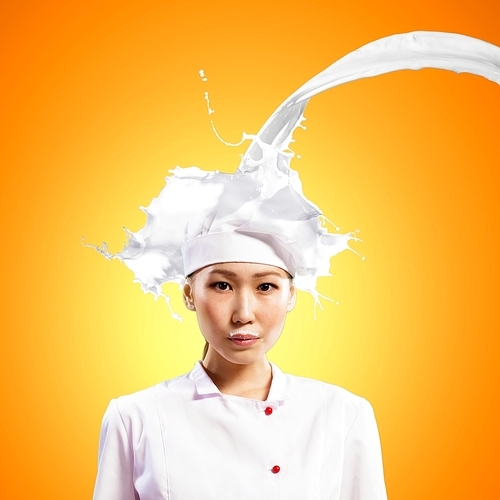 Asian female cook standing against milk splashes in red apron against colo:_x0004_ background