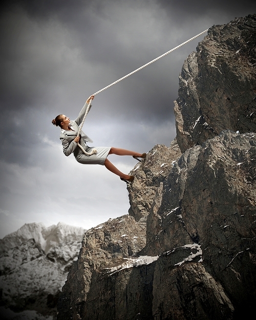 businesswoman climbing steep mountain hanging on rope