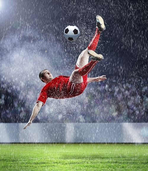 football player in red shirt striking the ball at the stadium under rain