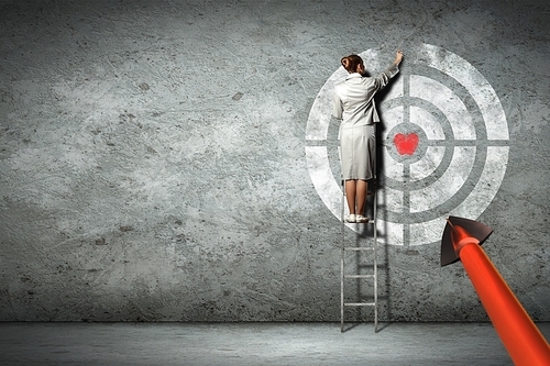 Businesswoman standing on ladder and pointing at target on wall