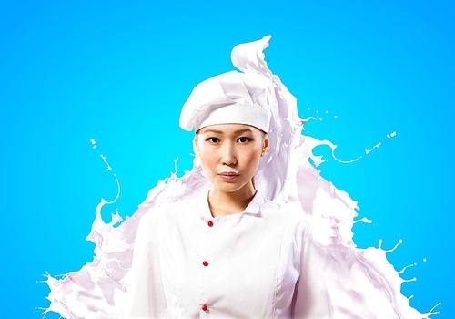 Asian female cook standing against milk splashes in red apron against colo:_x0004_ background