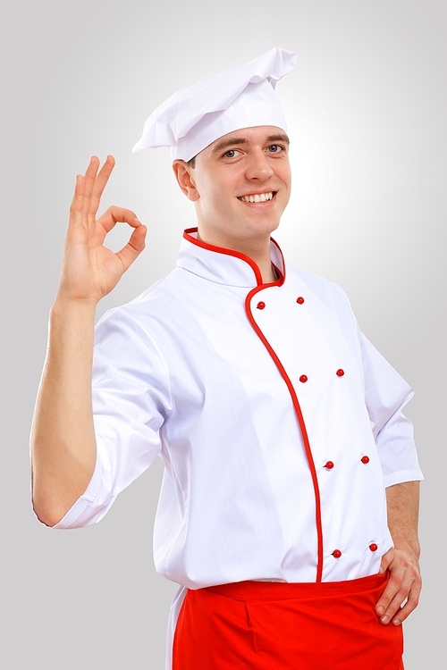 Young male chef in red apron against grey background