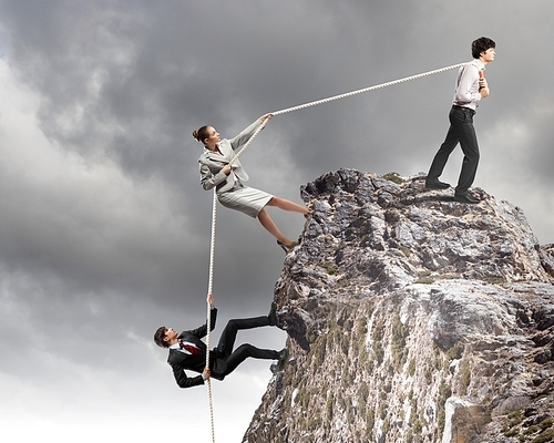 Image of three businesspeople pulling rope atop of mountain